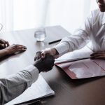 Duas pessoas apertam as mãos sobre um contrato durante uma negociação profissional