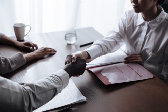 Duas pessoas apertam as mãos sobre um contrato durante uma negociação profissional