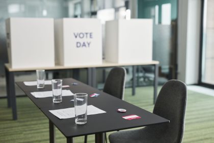 Sala preparada para votação, com mesas, cadeiras e cabines de privacidade organizadas para uma eleição.