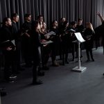 Coral de adultos ensaia em ambiente fechado sob a orientação de um maestro.
