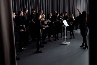 Coral de adultos ensaia em ambiente fechado sob a orientação de um maestro.