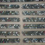 Vista aérea de um pátio organizado com numerosos veículos estacionados em fileiras.