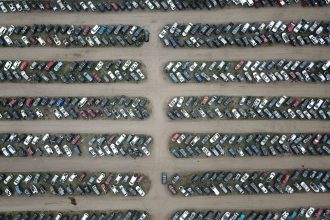 Vista aérea de um pátio organizado com numerosos veículos estacionados em fileiras.