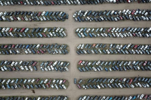 Vista aérea de um pátio organizado com numerosos veículos estacionados em fileiras.