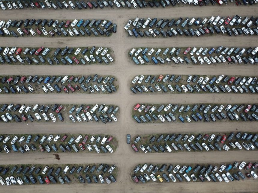 Vista aérea de um pátio organizado com numerosos veículos estacionados em fileiras.