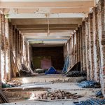 Interior vazio de um edifício em reforma, com tijolos aparentes e materiais de construção espalhados pelo espaço.