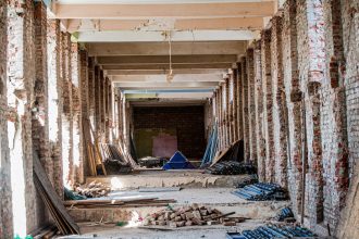 Interior vazio de um edifício em reforma, com tijolos aparentes e materiais de construção espalhados pelo espaço.