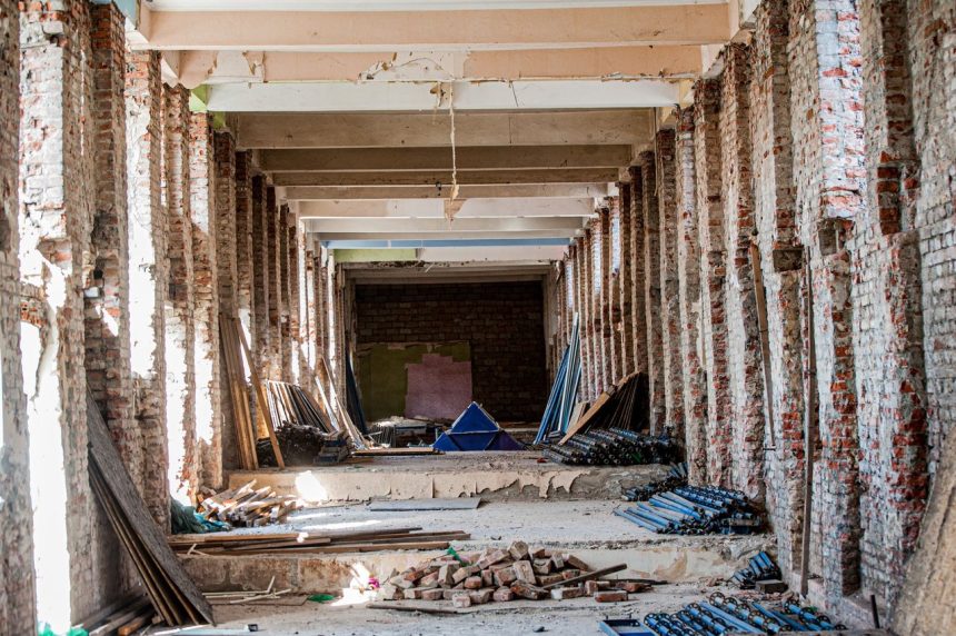 Interior vazio de um edifício em reforma, com tijolos aparentes e materiais de construção espalhados pelo espaço.
