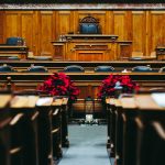 Interior amplo de uma sala de tribunal vazia, com bancos e mobiliário de madeira.