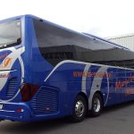 Ônibus rodoviário azul estacionado ao ar livre sob um céu parcialmente nublado.