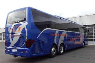 Ônibus rodoviário azul estacionado ao ar livre sob um céu parcialmente nublado.